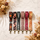 Set of six patterned keychains on a marble surface with dried flowers.