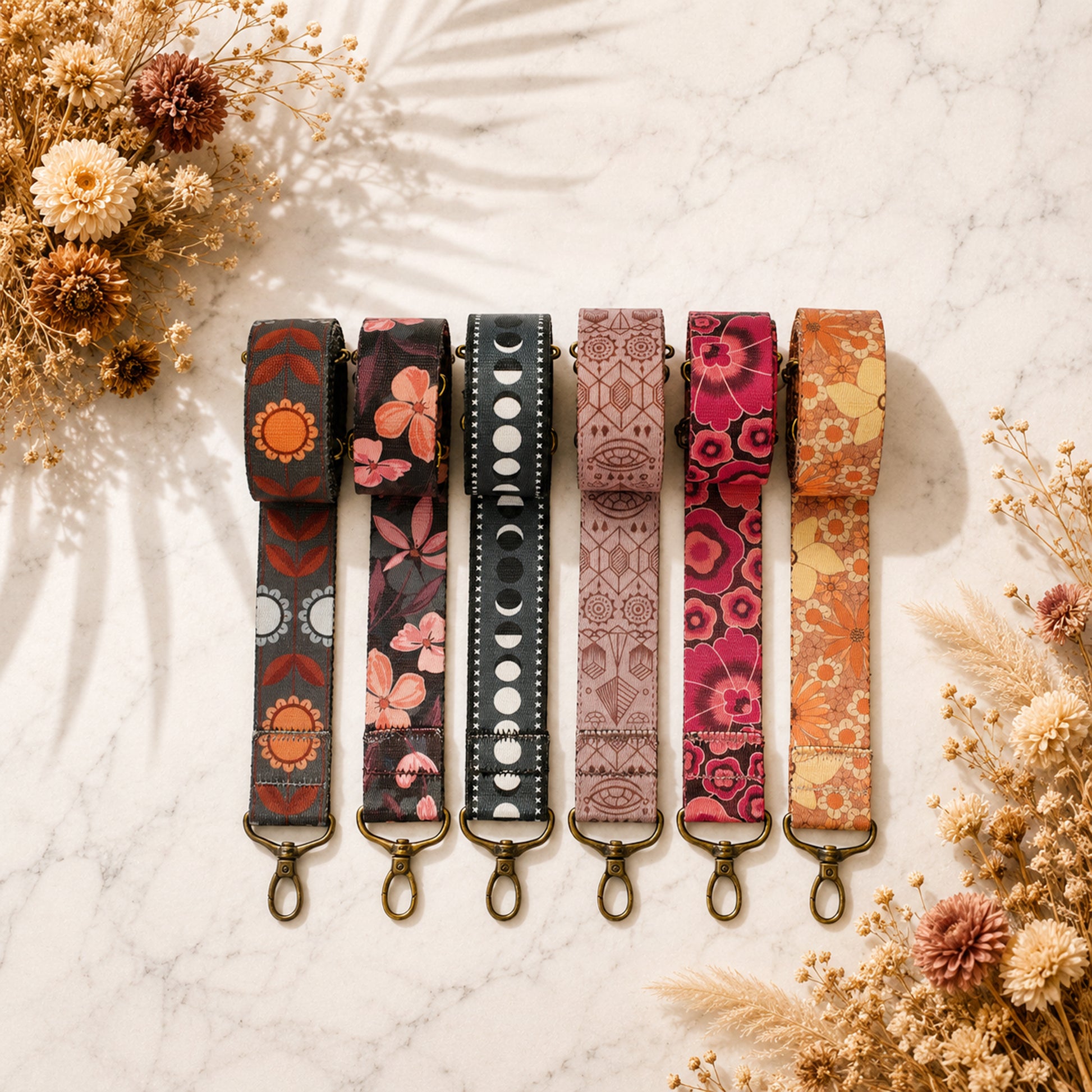 Set of six patterned keychains on a marble surface with dried flowers.