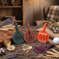 Personalized leather golf keychains and matching accessories displayed on a rustic wooden table with dried wheat, lavender, a compass, and a golf ball. The set includes a green octagonal keychain engraved with 'HARRY', a brown octagonal keychain engraved with 'ARL', an orange set of golf tees, a purple tee pad, and a brown leather bag.