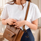 Person holding a brown leather bag with a neutral background