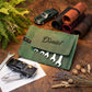 A personalized green leather tool roll with the name 'Daniel' stitched on the flap, displayed on a wooden table with wrenches, a toy car, rolled leather sleeves, and decorative plants.