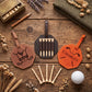 A golf accessory set arranged on a rustic wooden surface, including two personalized leather golf tees or clubs holders engraved with names, a central black holder with five wooden tees, additional wooden tees, a golf ball, dried flowers, a pencil, a small metal case, and a folded herringbone fabric.
