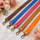 Five colorful leather straps with metal hooks on a marble surface with flowers.