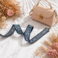 Beige handbag with a floral strap on a marble surface with dried flowers.