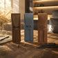 Three personalized leather pen sleeves standing on a wooden table in a warm, sunlit room. The left sleeve is brown with the name 'Kevin' in black script, the center sleeve is light blue with 'M.
