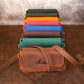 Brown leather bag with 'Maria' branding in front of colorful fabric rolls on a brown surface.