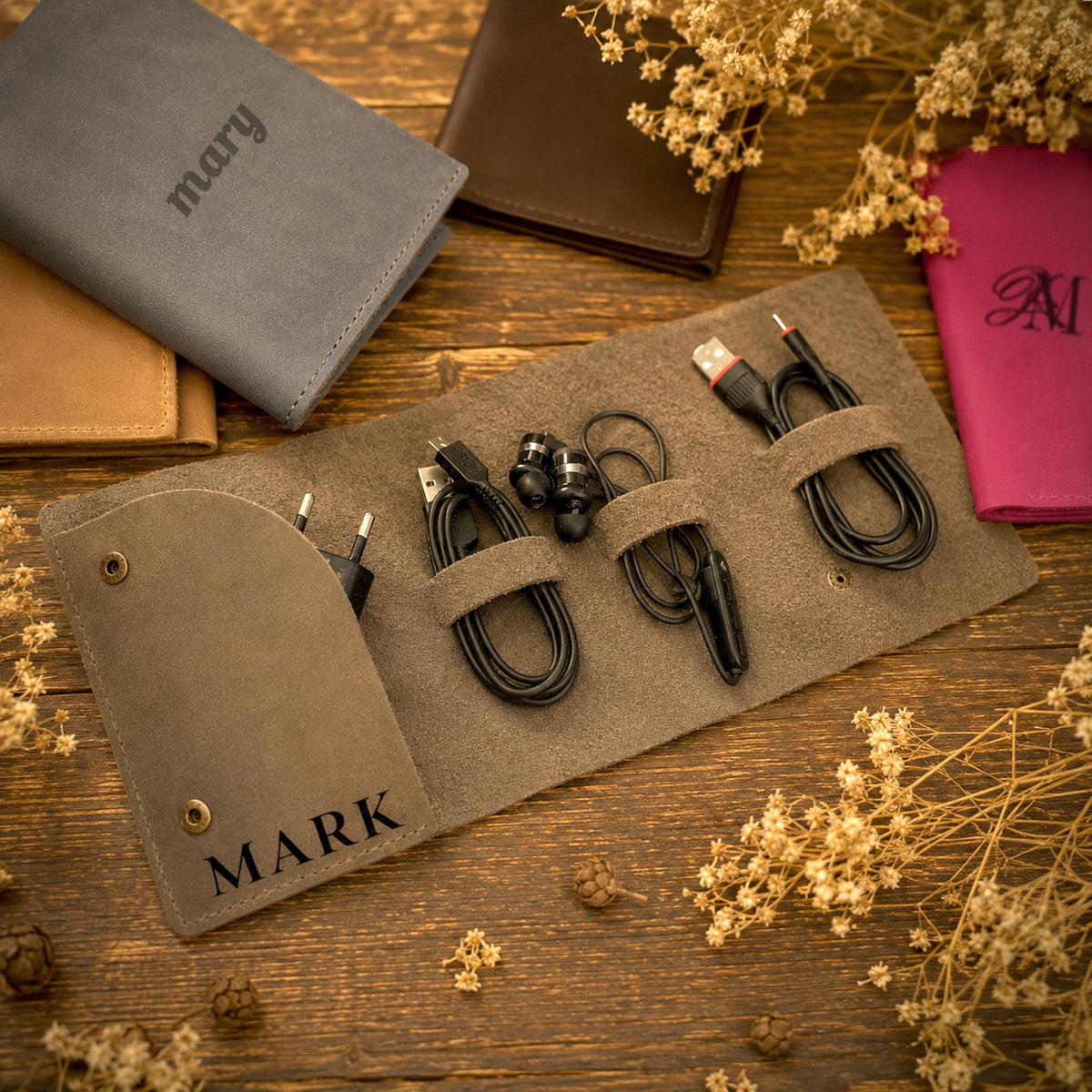 A styled flat-lay of several leather wallets and card holders arranged on a rustic wooden surface with dried flowers, rope, and pinecones.