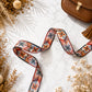 Decorative ribbon with geometric pattern on a textured surface with dried flowers and a brown bag.