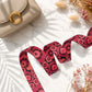 Beige handbag with a red floral strap on a marble surface with dried flowers.