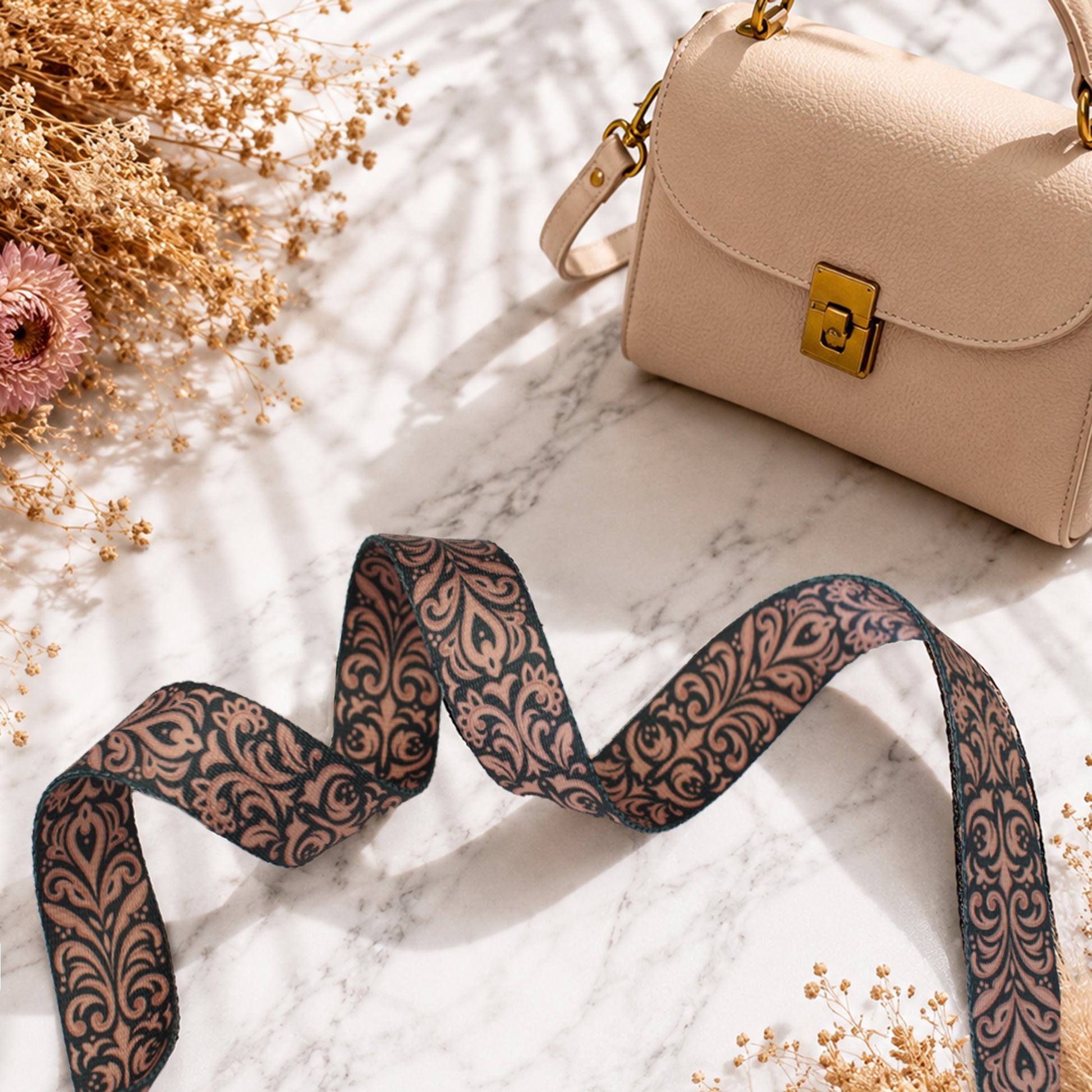Beige handbag with a decorative strap on a marble surface with flowers.