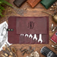 A maroon leather tool roll with a monogrammed 'JKF' flap, displayed in a styled flat-lay on a wooden surface with wrenches visible in the pockets and automotive-themed props around it.