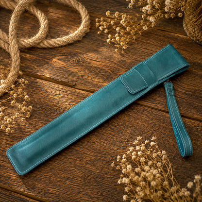 A teal blue leather strap or belt laid diagonally on a rustic wooden surface, surrounded by dried flowers and a coiled rope.