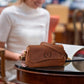 Brown leather handbag on a table with a blurred person in the background