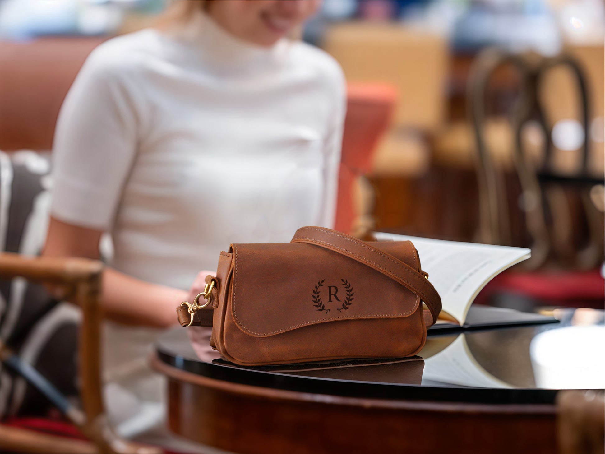 Brown leather handbag on a table with a blurred person in the background