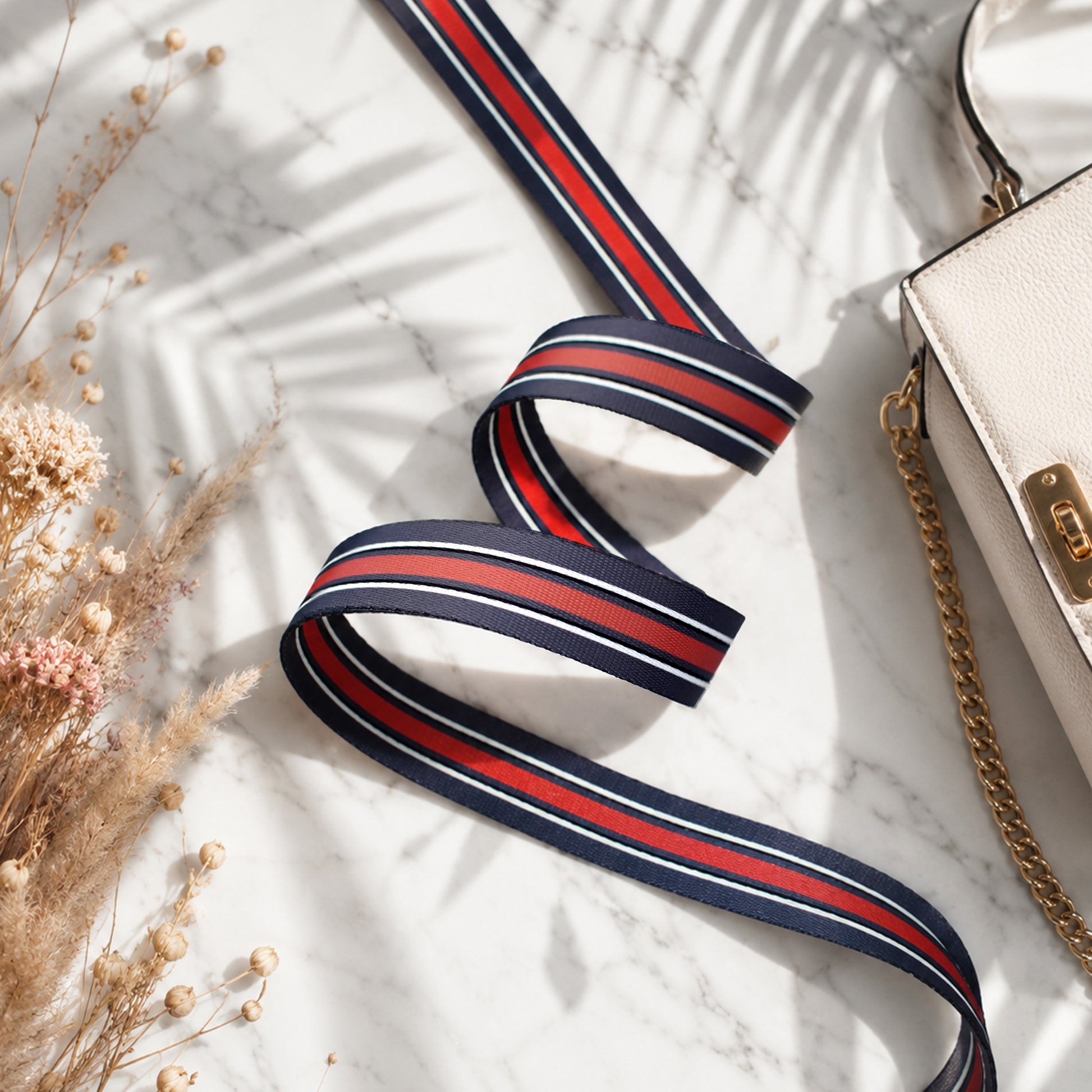 Striped ribbon with red and blue stripes on a light surface with a handbag and dried flowers.