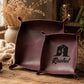 Two square dark burgundy leather storage bins with handles, one plain and one personalized with a black house silhouette and the name Rachel, displayed on a rustic wooden table with dried flowers and a cozy background.