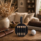 A black leather golf teiger set holder with five wooden teiger sticks, displayed on a rustic wooden table next to a golf ball, a brown leather notebook, and a vase of dried grasses in a cozy living room setting.