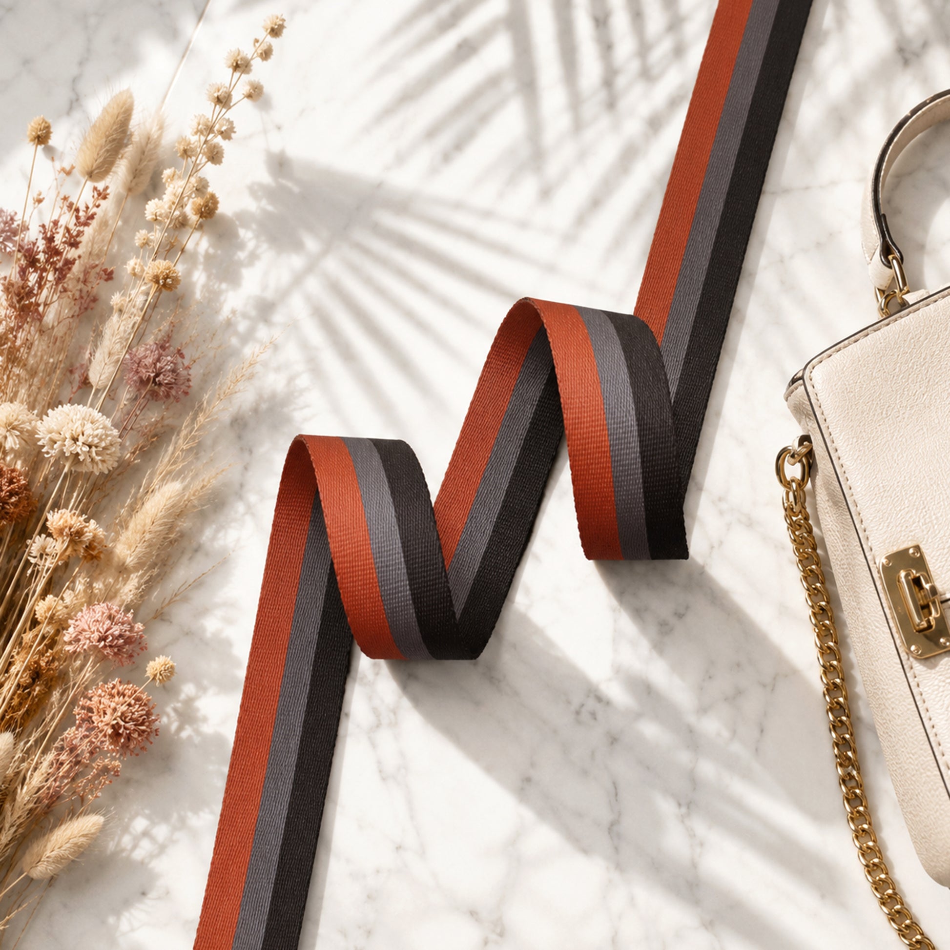 Striped ribbon with dried flowers and a handbag on a light surface