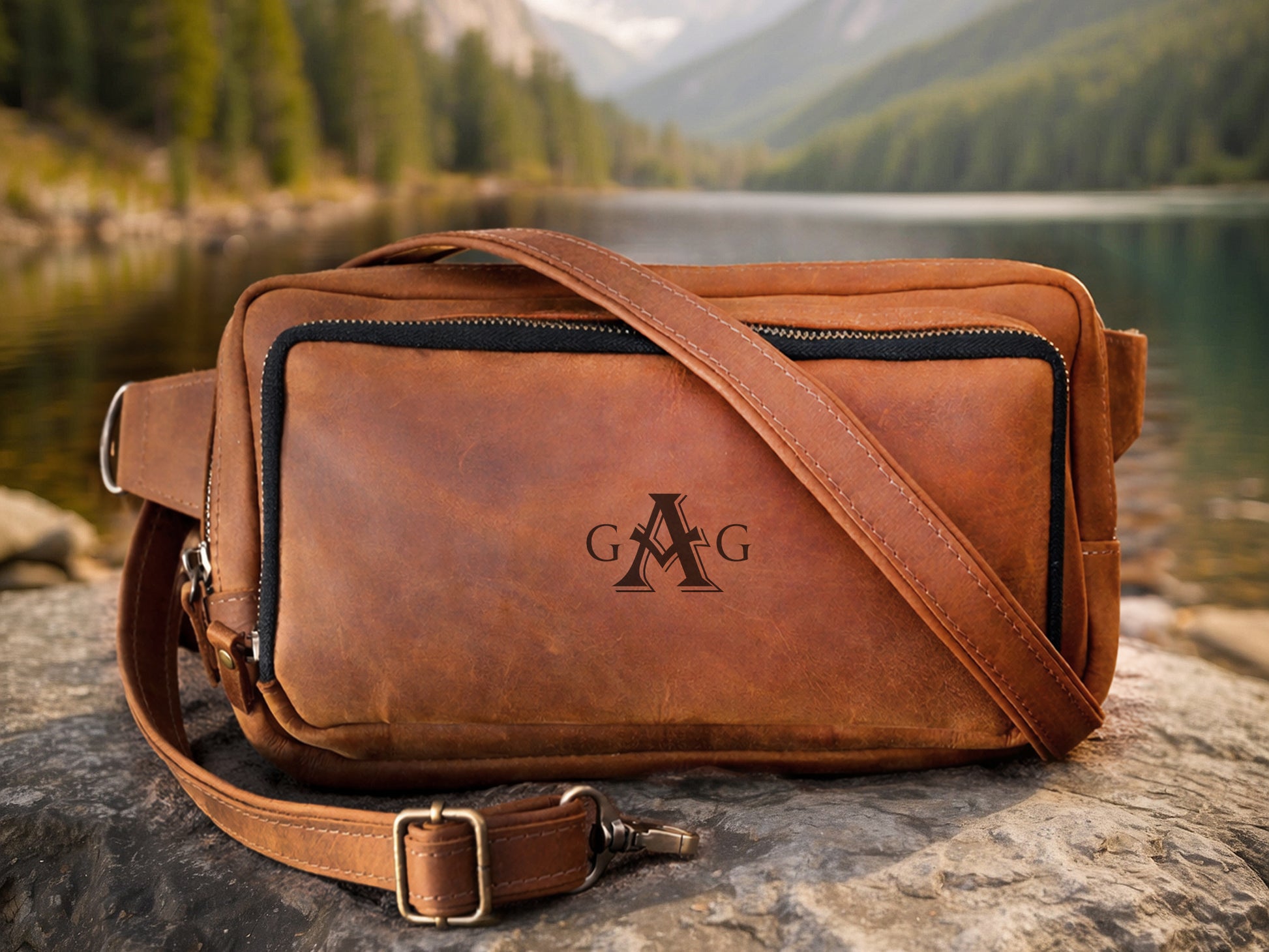 Brown leather bag with a visible brand logo on a rock by a lake with mountains in the background