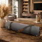 A rolled gray yoga mat with an olive green carrying strap and a small tan leather brand tag reading 'YOGA' in a warm, modern living room setting.