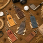 Six personalized leather golf keychains arranged on a wooden tabletop with golf-themed props including a golf club, golf ball, camera, and rope.
