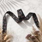 Black ribbon with red pattern on a light background with dried plants