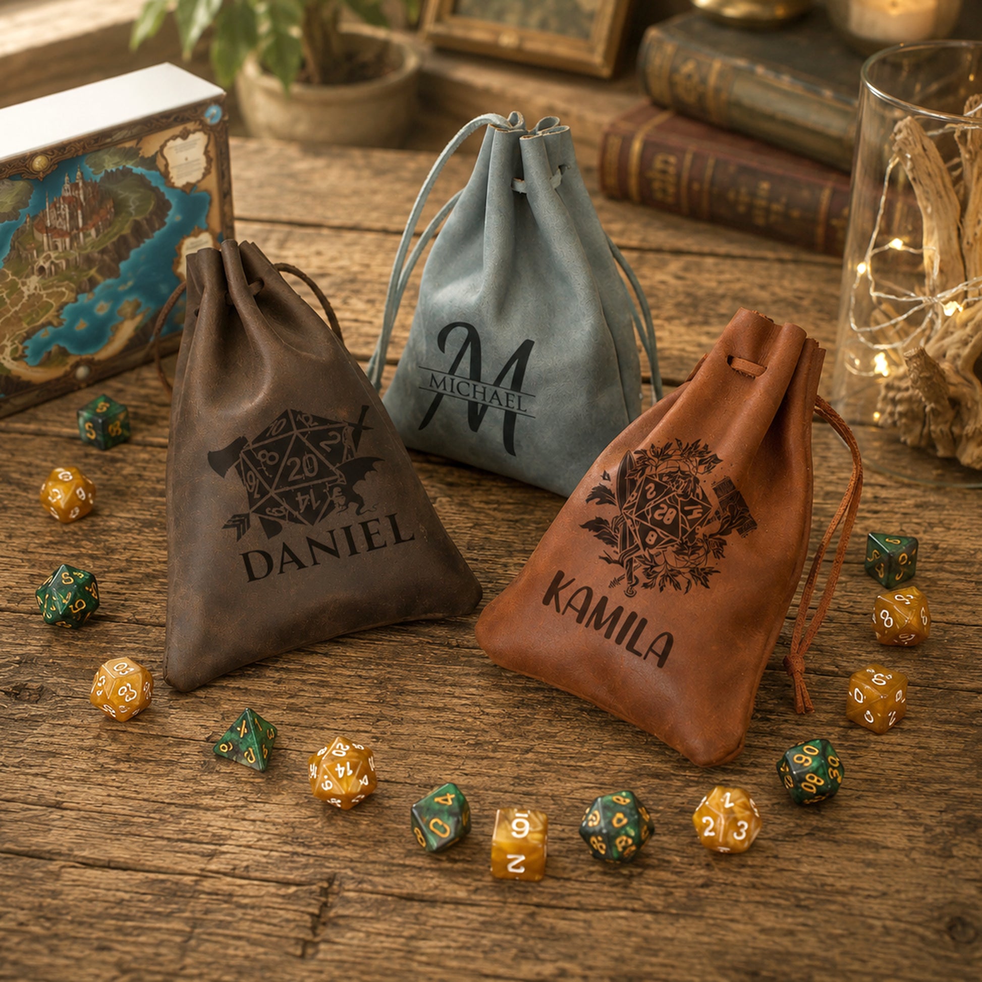 Three personalized drawstring pouches on a rustic wooden table, surrounded by polyhedral gaming dice. The pouches are made of different materials: a dark brown leather pouch labeled 'DANIEL', a light blue faux-leather pouch labeled 'M.