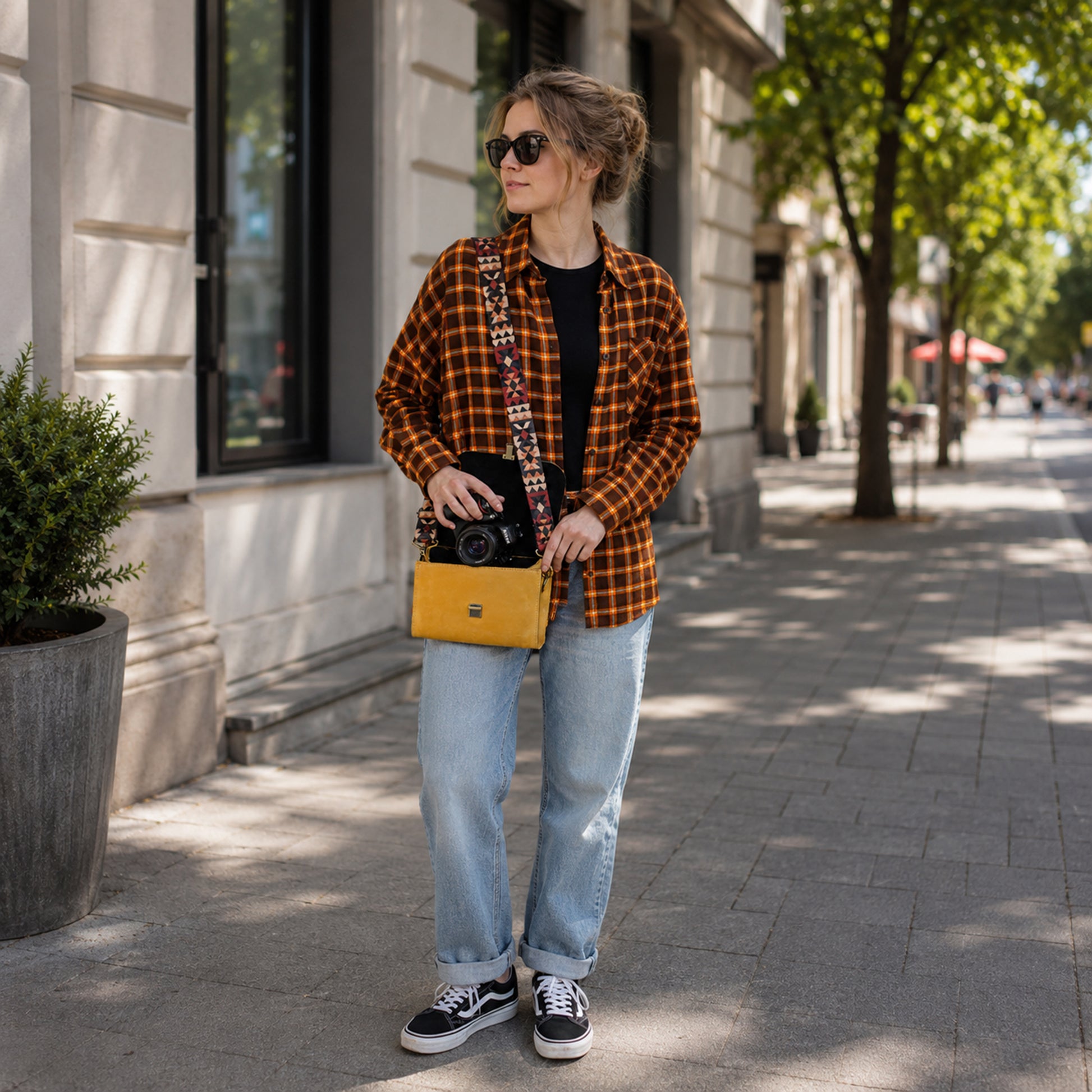 Woman in plaid shirt and jeans standing on a sidewalk with a yellow bag.