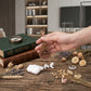 A hand holds a brown leather keychain with the name 'Darren' engraved on a round tag, shown in a styled indoor setting with books, dried flowers, and white wireless earbuds nearby.