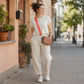 Woman walking on a sidewalk with a pink bag and white outfit