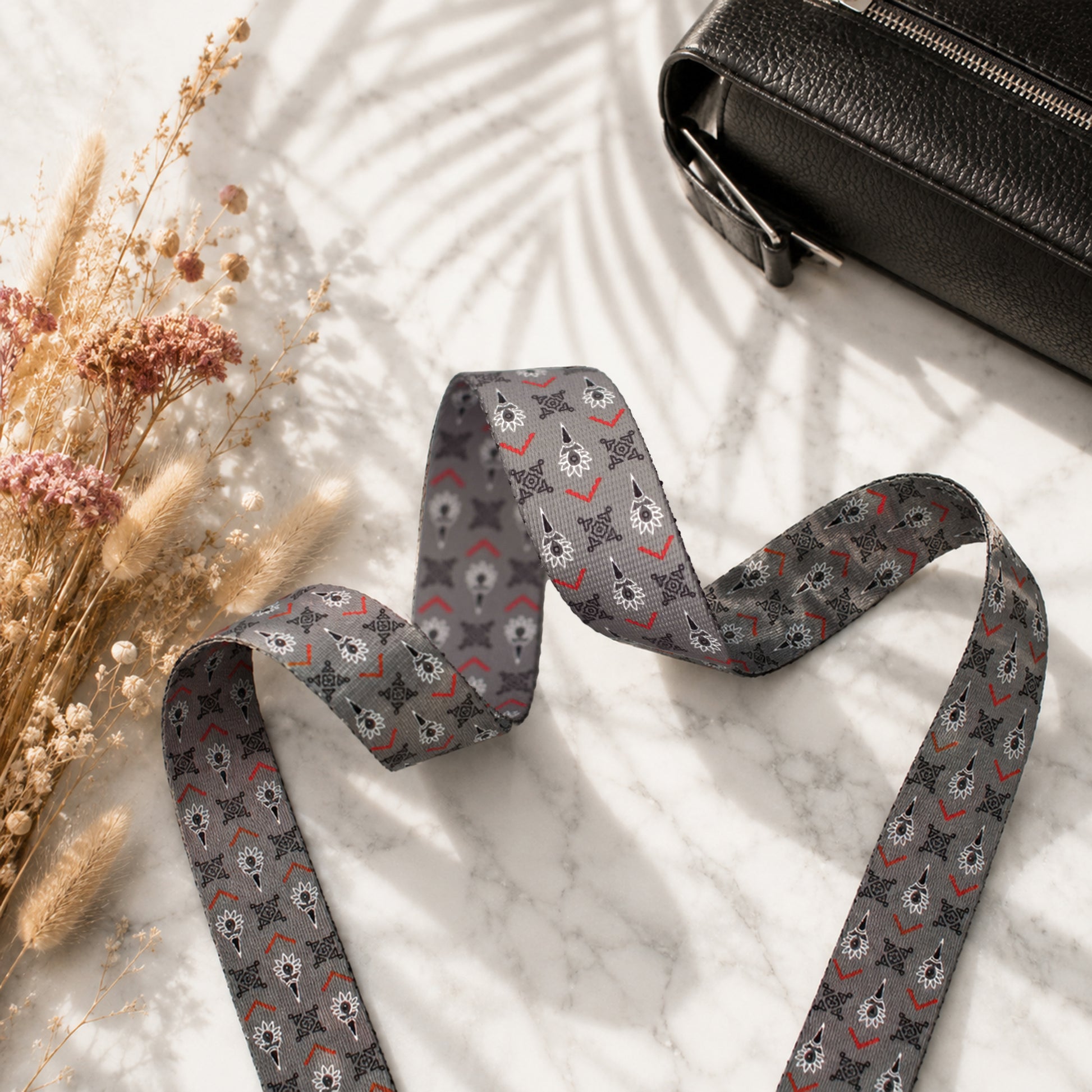 Patterned strap on a marble surface with dried flowers and a black bag.