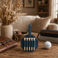 A dark teal leather golf tees holder containing five wooden golf tees, displayed on a rustic wooden table with a golf ball, a notebook, and a book in a cozy, warm-toned room setting.