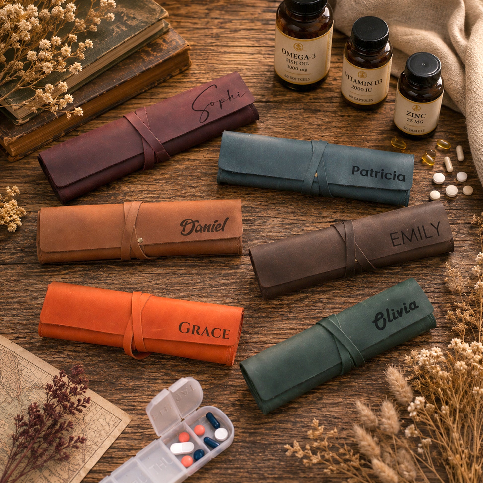 Six personalized leather pill organizer rolls in assorted colors, each rolled and stamped with a name (Sophia, Patricia, Daniel, Emily, Grace, Olivia), arranged on a rustic wooden table alongside supplement bottles, dried flowers, and an open pill box.