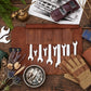 A leather wrench roll with multiple silver wrenches laid out on a rustic wooden table, surrounded by workshop-themed props including gloves, a brass oil can, wrenches, dried flowers, and a toy car. The leather roll is personalized with the initials 'JKF'.