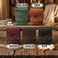 Six leather pouches or small cases shown in different colors on a rustic wooden table: dark green, tawny, burgundy, chocolate, and black. Each has a flap closure with two brass-tone studs and a rectangular cutout.