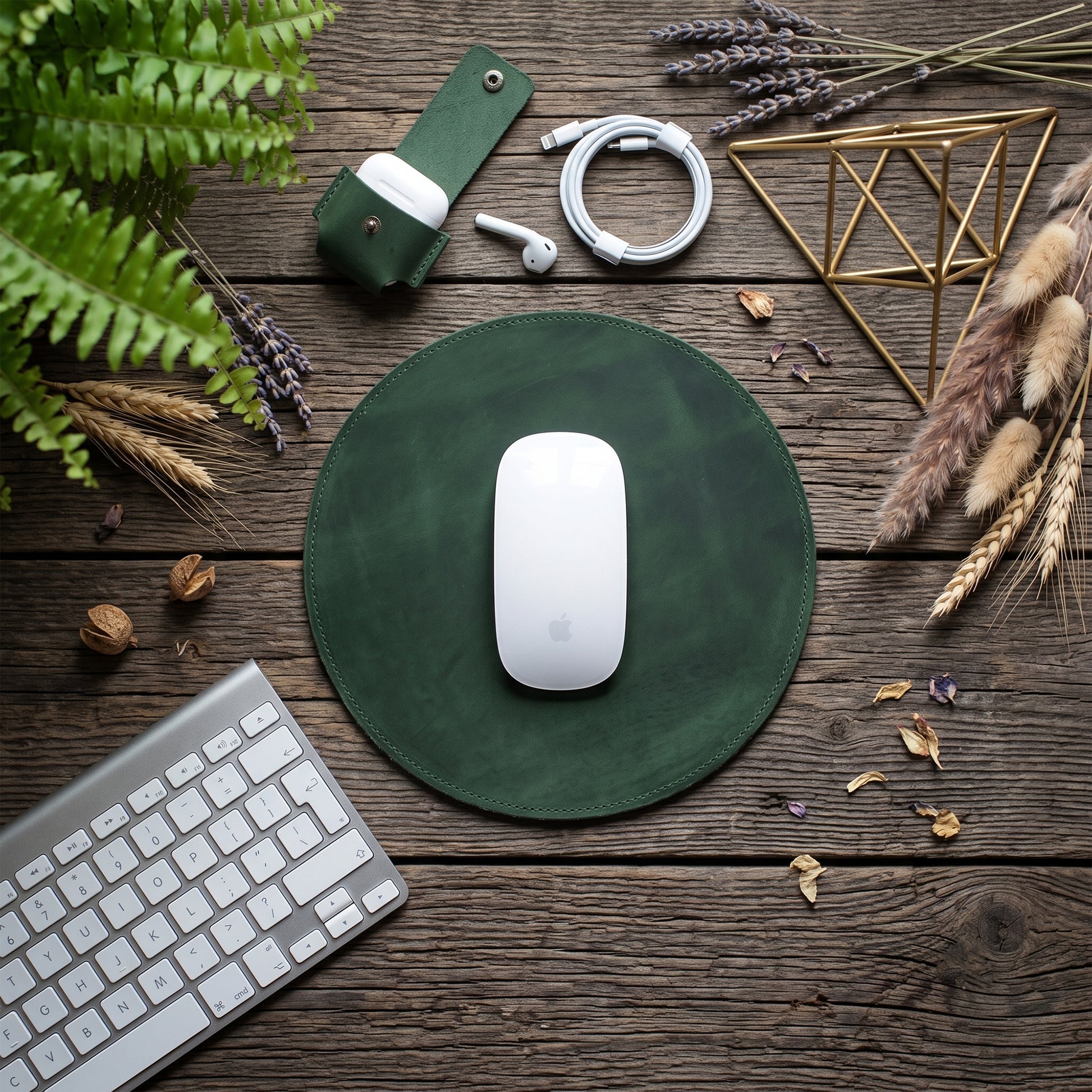 A dark green round mouse pad with a white Apple Magic Mouse on top, styled in a flat-lay on a rustic wooden table with a keyboard, earbuds, and dried plants.