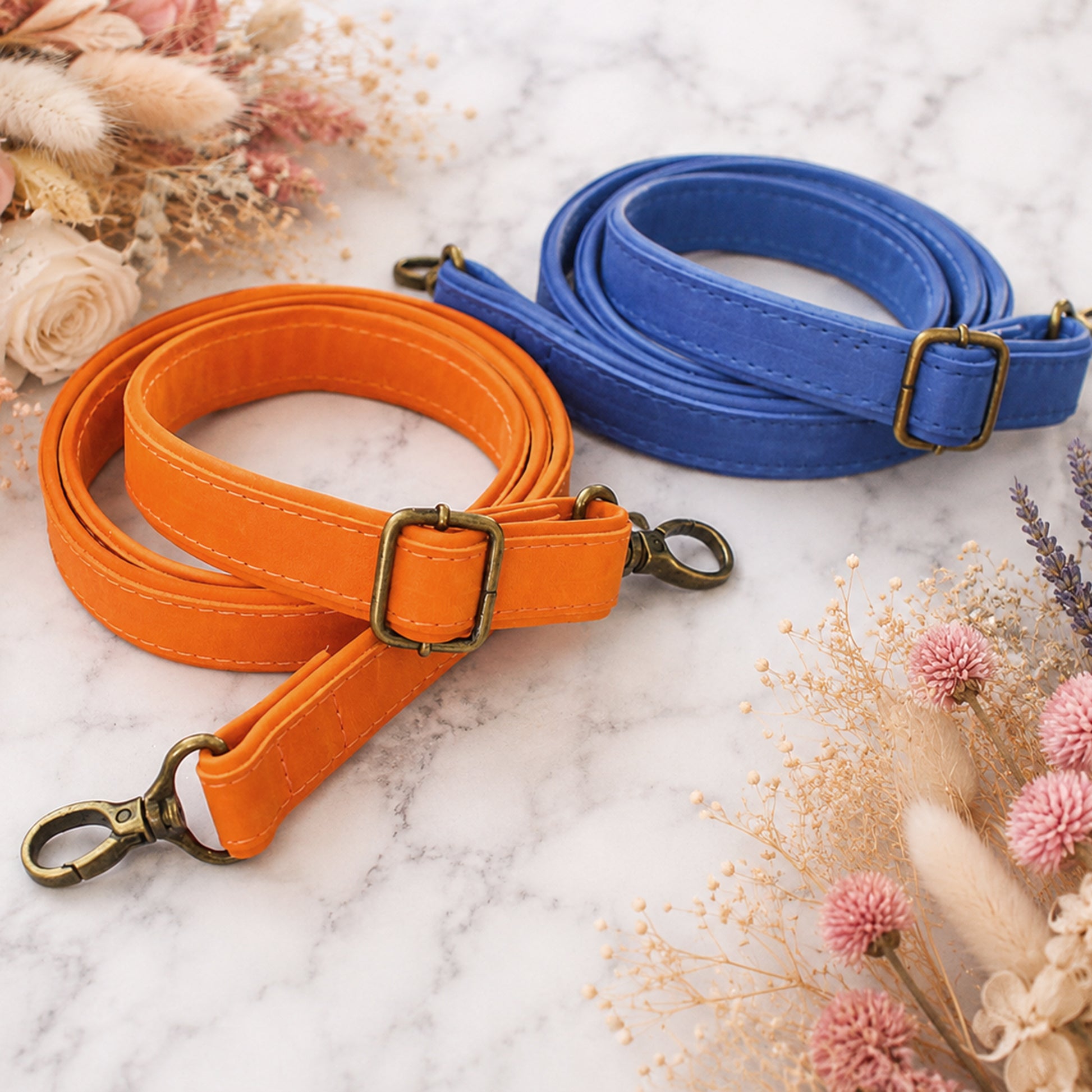 Orange and blue dog leashes with brass buckles on a marble surface with dried flowers.