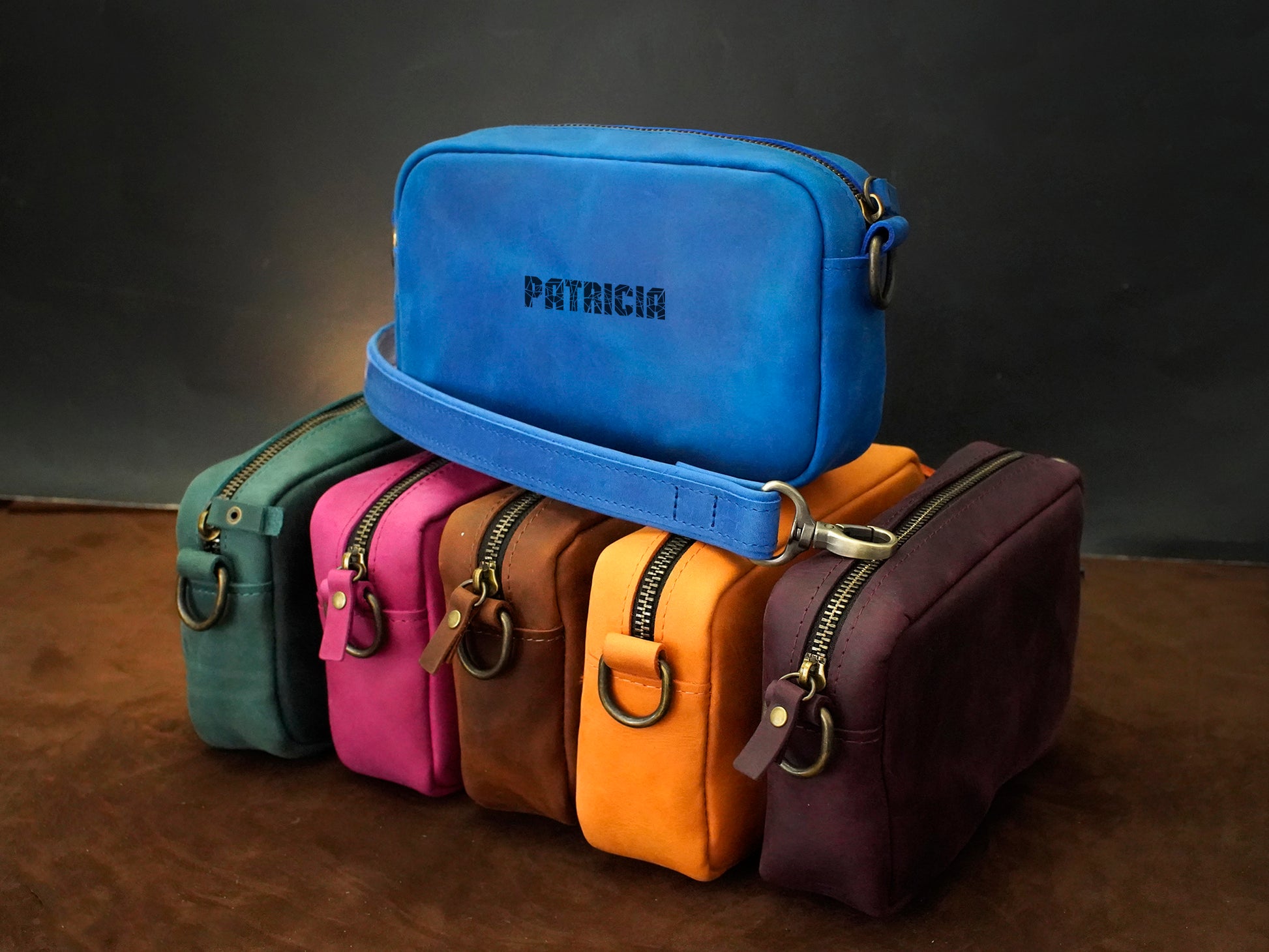 Stack of colorful leather bags with 'Patricia' branding on a dark background