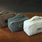 Three textured toiletry bags with visible branding on a brown surface.