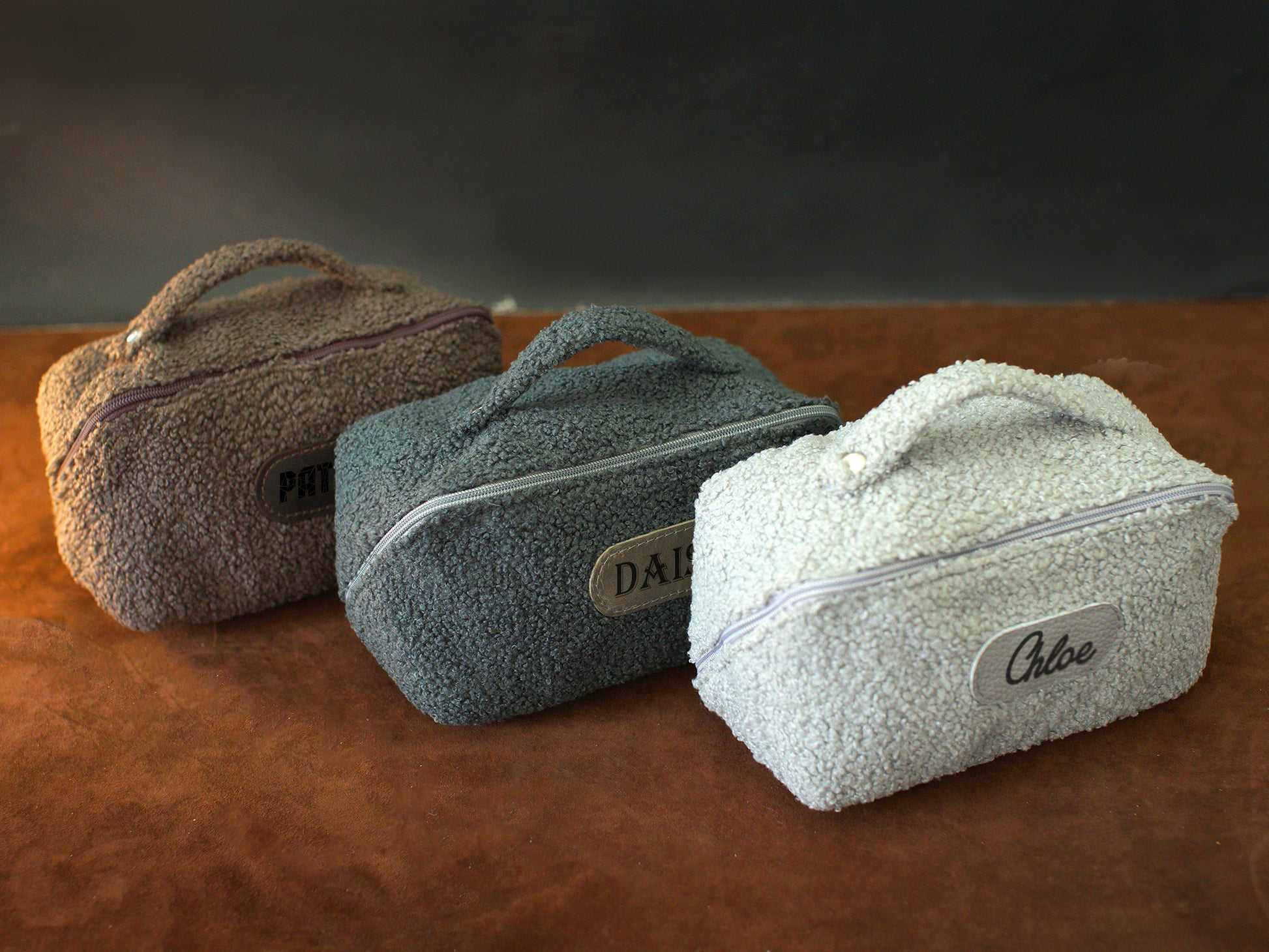 Three textured toiletry bags with visible branding on a brown surface.