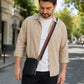 Man walking outdoors wearing a beige shirt with a black crossbody bag