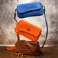 Three handbags stacked on a textured surface with a neutral background