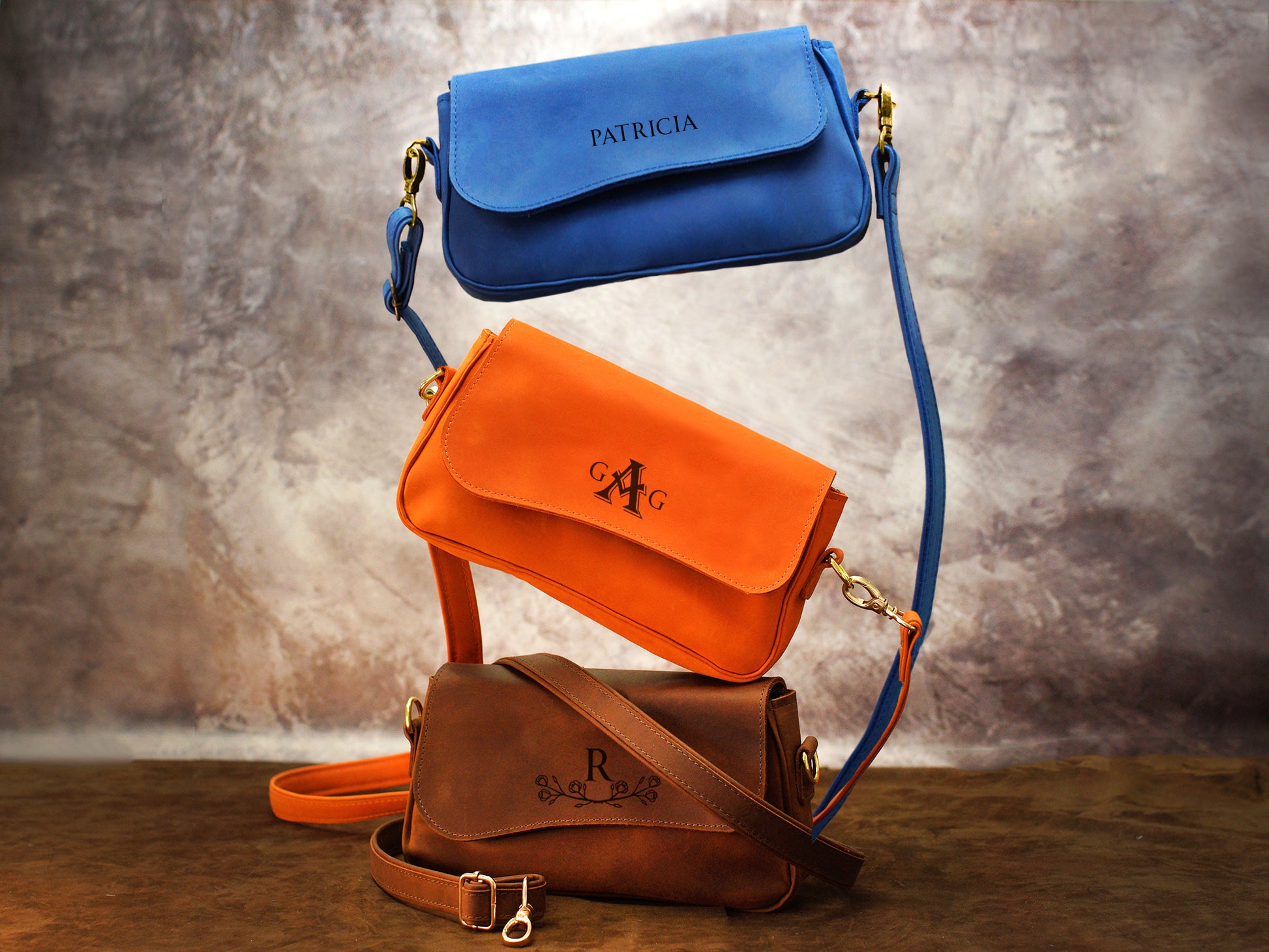 Three handbags stacked on a textured surface with a neutral background