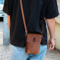 Person wearing a brown leather crossbody bag with a visible brand logo on a street.
