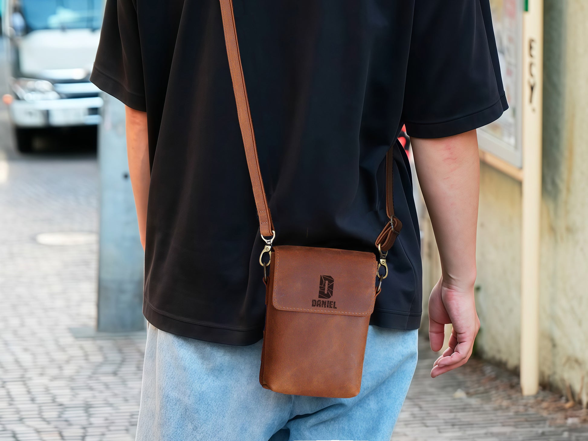 Person wearing a brown leather crossbody bag with a visible brand logo on a street.