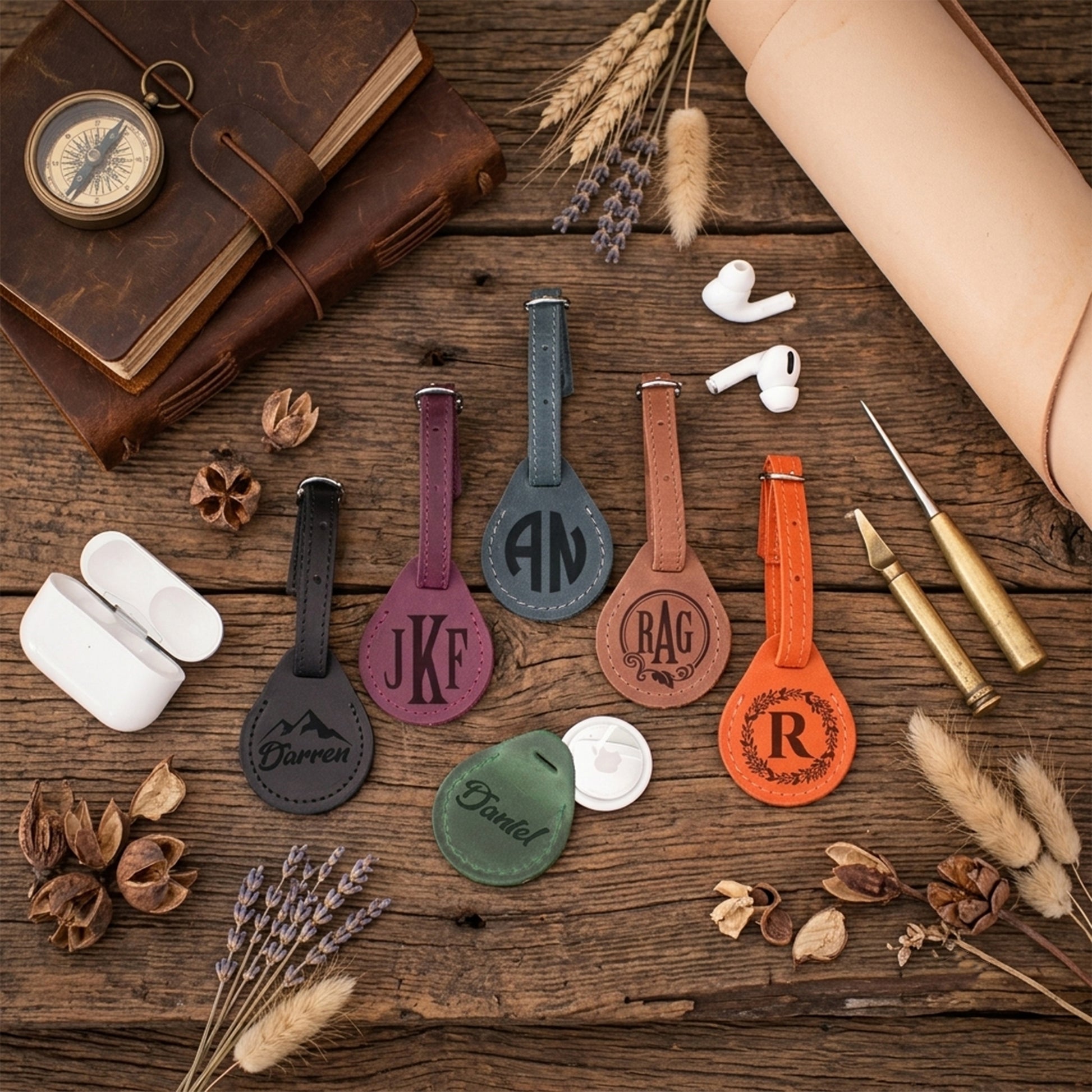 Five personalized leather luggage tags in different colors (black, purple, blue-gray, brown, green, and orange) with monogrammed initials, arranged on a rustic wooden table with travel-themed props like a compass, leather journal, earbuds, and dried lavender.