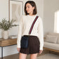 Woman in a living room wearing a cream sweater and brown skirt with a black bag.
