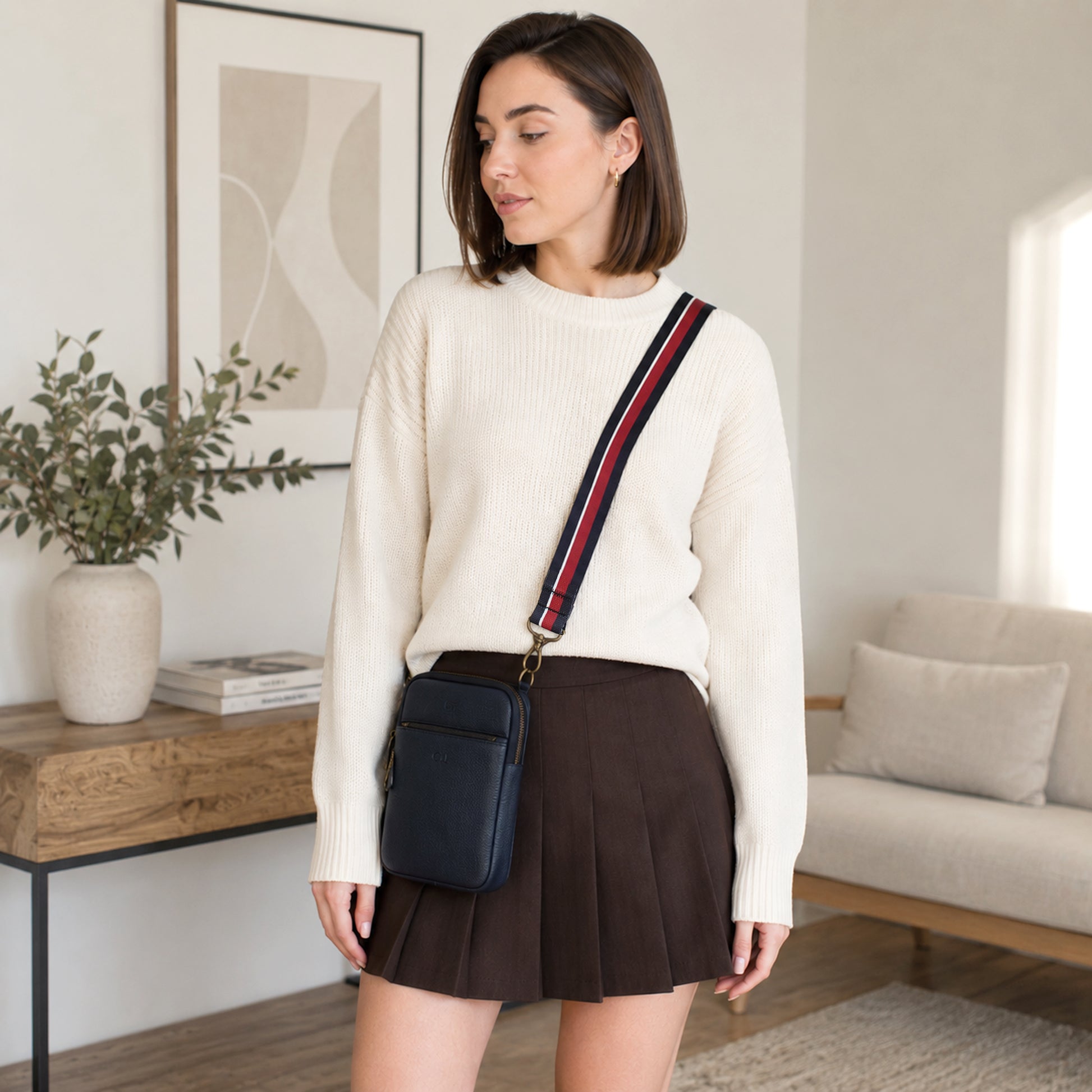 Woman in a living room wearing a cream sweater and brown skirt with a black bag.