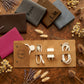 A tan roll-up organizer case laid flat on a wooden surface, holding white charging cables, a power adapter, and a round magnetic accessory. Several personalized wallet-style cases in brown, gray, blue, and pink are arranged around it with dried flowers as styling props.