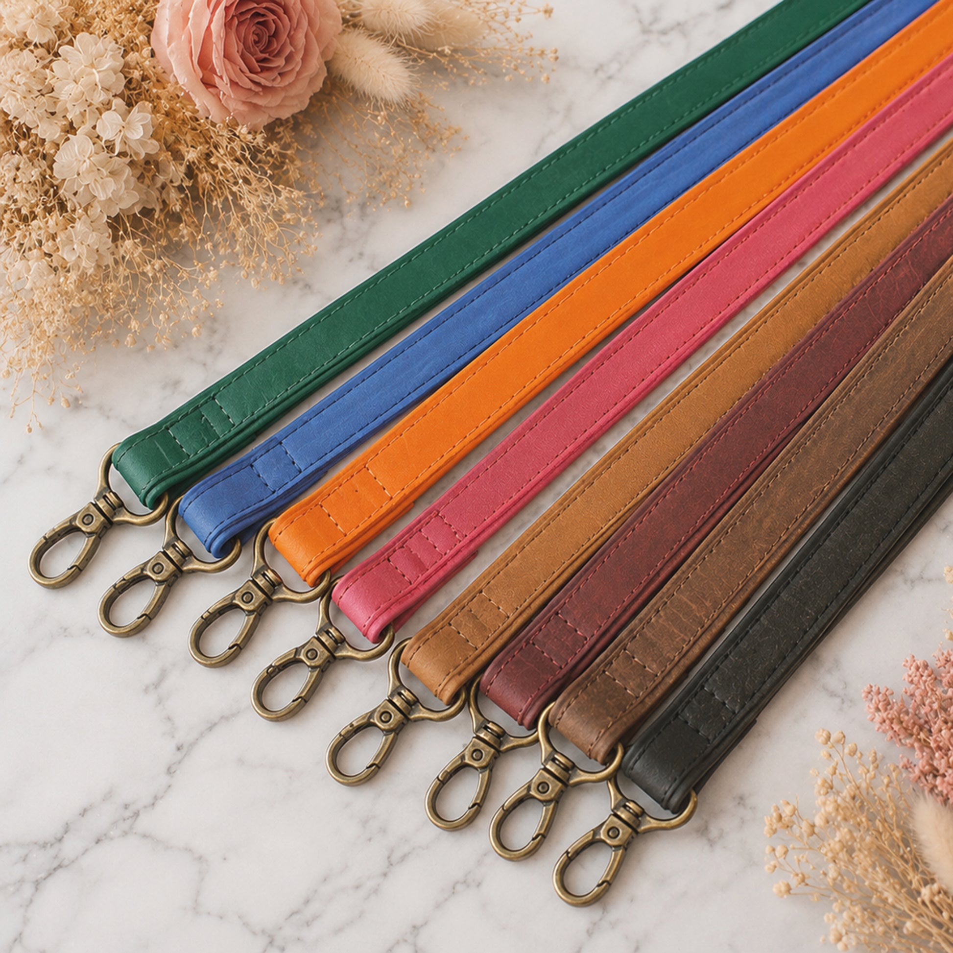 Set of colorful leather straps with metal hooks on a marble surface with flowers.